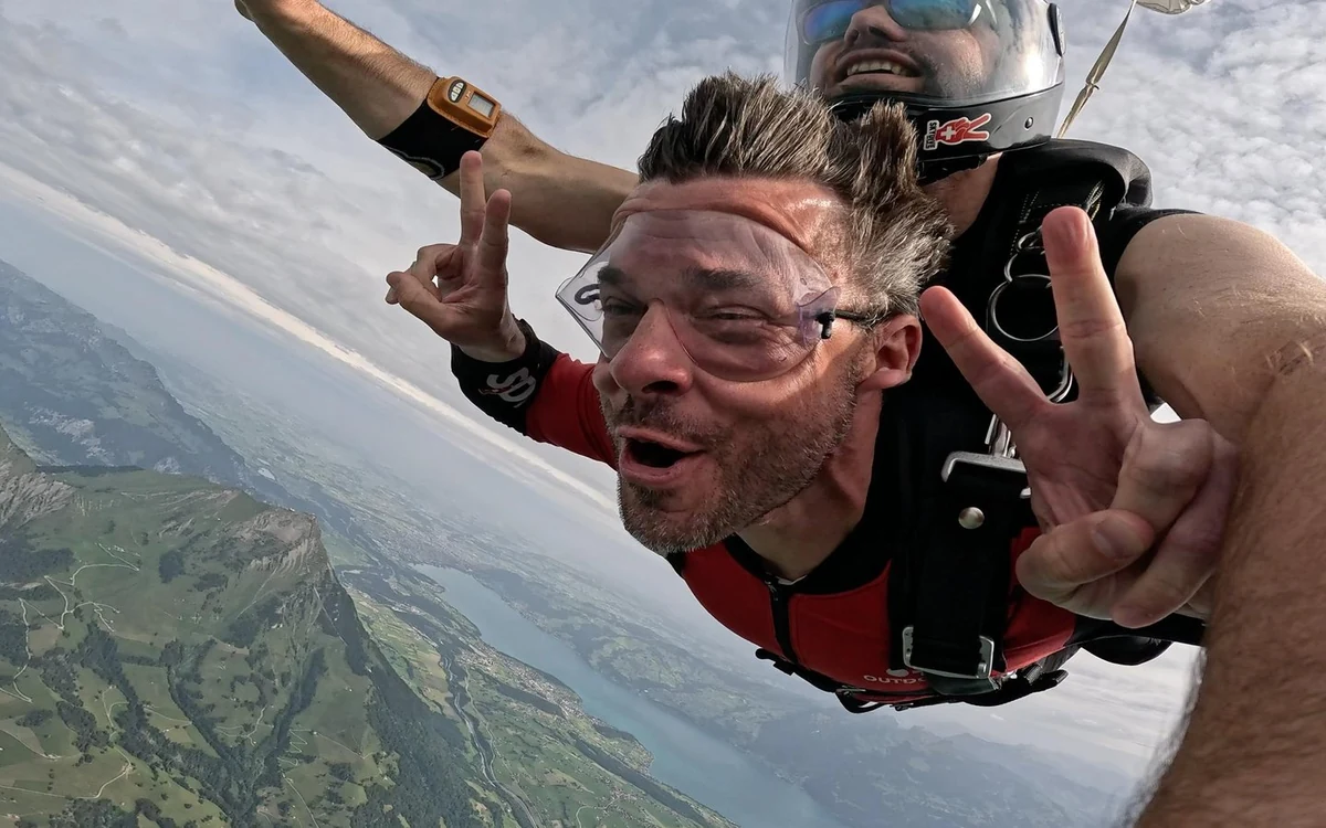 A tandem skydiver under an open canopy above the valley near Interlaken