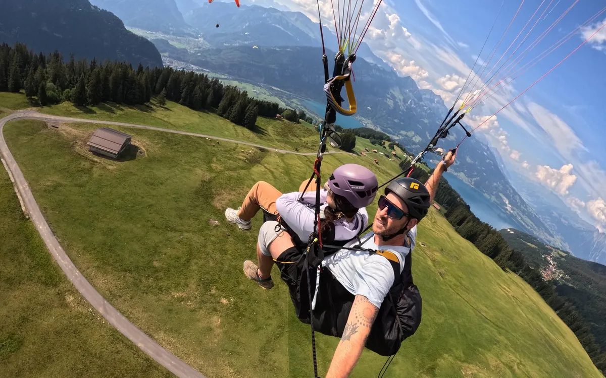 An open parachute canopy above the green Interlaken valley between its two lakes